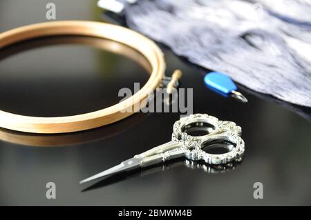 Accessories for needlework. Hoop, multi-colored threads, scissors, needle-threader on a black background. Copy space. Stock Photo