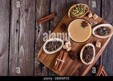 Traditional Indian drink - masala tea with spices. Cinnamon, cardamom, anise, sugar, cloves, pepper on a dark wooden background. Copy space. Flat lay. Stock Photo