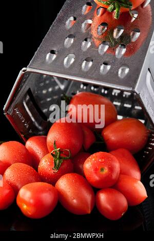Culinary concept. Large tomato and grater down to small grape cherry tomatoes on a black background. Low calorie food. Stock Photo