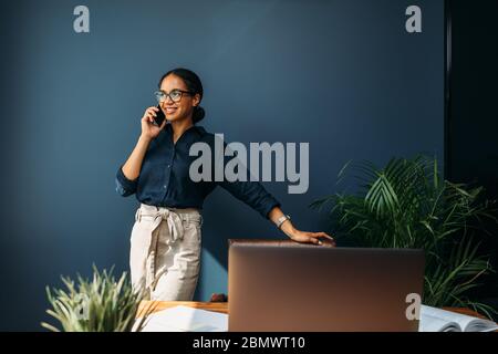 Happy entrepreneur leaning to a chair and looking away while talking on mobile phone Stock Photo