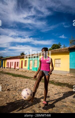 Girl playing football  against the background of colourful houses in the colonial era centre of the town, Trinidad, Cuba Stock Photo