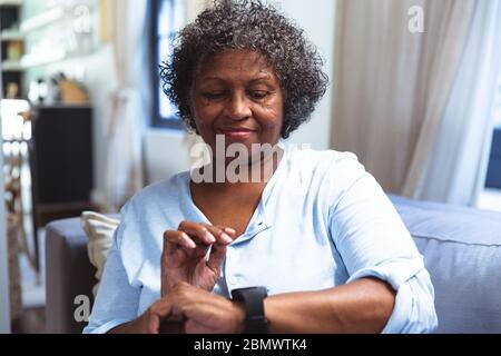 Senior African American woman using digital watch at home during quarantine lock down for coronaviru Stock Photo