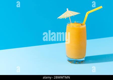 Glass of mango smoothie with summer decor on a blue background, in harsh light. Healthy smoothie drink. Vitamin breakfast beverage. Dietary mocktail. Stock Photo