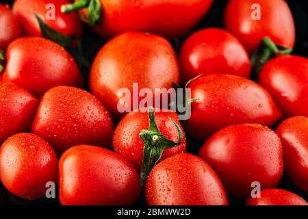 Big tomato and small grape cherry tomatoes on a black background. Low calorie food. Stock Photo