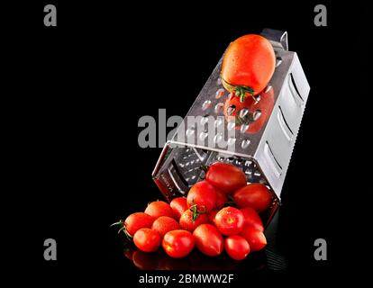 Culinary concept. Large tomato and grater down to small grape cherry tomatoes on a black background. Low calorie food. Stock Photo