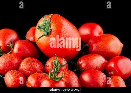 Big tomato and small grape cherry tomatoes on a black background. Low calorie food. Stock Photo