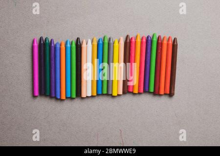 many multi-colored wax crayons on grey paper. Flat lay Stock Photo