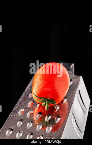 Culinary concept. Large tomato and grater on a black background. Low calorie food. Stock Photo