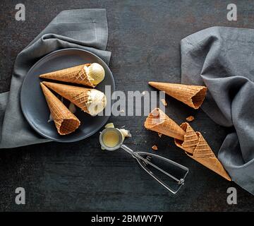Vanilla ice cream scoops, scooped from container in to waffle cones with a silver utensil Stock Photo