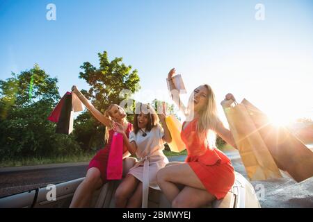 Sale, consumerism: Multi ethnic group of girls rides on convertible car cabriolet with shopping bags after visiting mall Stock Photo