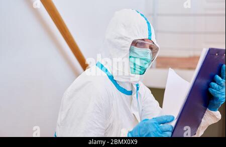 Containtment scout in protective clothing looks at list for contact tracking in coronavirus pandemic Stock Photo