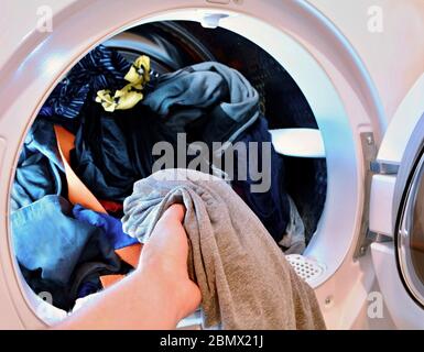 Closeup of hand holding and put washed laundry into tumble clothes dryer machine. Stock Photo