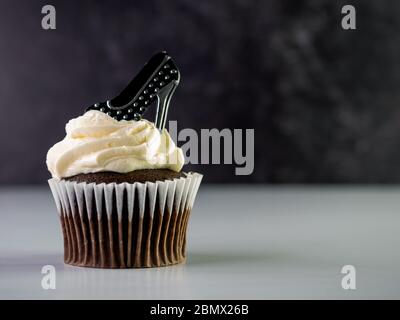 Chocolate cupcake with white frosting swirled up high and a black and silver polka dot high heel sitting on top with a white counter and black marble Stock Photo
