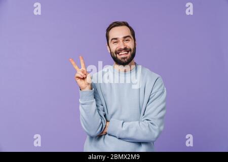 Image of a handsome positive happy young man isolated over purple wall background showing peace gesture. Stock Photo