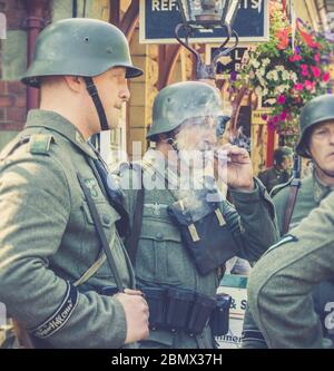 Retro view of Nazi soldiers in uniform chatting, relaxing at vintage train station, Severn Valley heritage railway 1940s WW2 WWII wartime summer event. Stock Photo