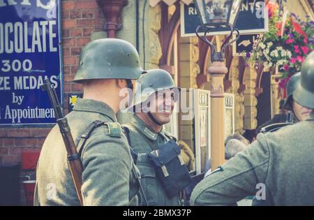 Retro view of Nazi soldiers in uniform chatting, relaxing at vintage train station, Severn Valley heritage railway 1940s WW2 WWII wartime summer event. Stock Photo