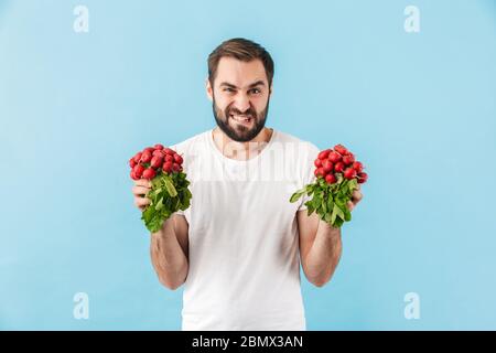 Portrait of a young angry disgusted bearded man wearing t-shirt standing isolated over blue background, showing fresh redish Stock Photo