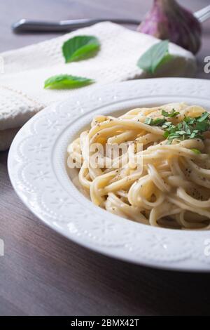 Vegan version of traditional italian pasta fettuccine alfredo with creamy white sauce garnished with basil on a wooden surface with a fork, napkin, ga Stock Photo