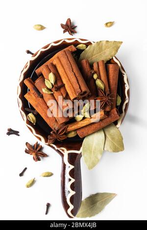 Healthy food ingredient mix of spices organic Cinnamon sticks, star anise, bay leaves and Cardamom pods in brown handle ceramic bowl on white backgrou Stock Photo