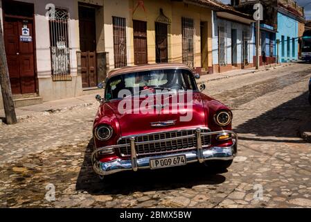 Classic car driving down a typical cobblestoned street with colourful houses in the colonial era centre of the town, Trinidad, Cuba Stock Photo