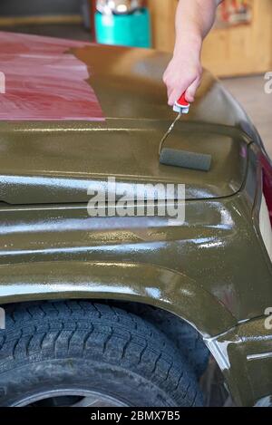 close up of a man painting an old jeep in army green with a paintbrush and paint Stock Photo