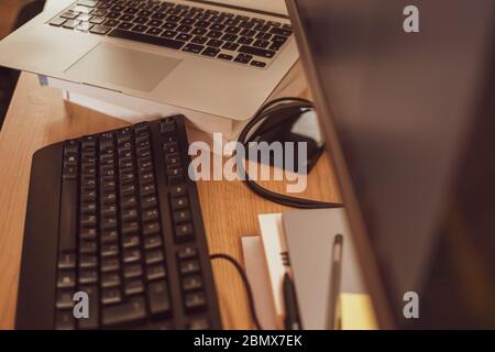 A busy modern home office set-up with a keyboard, laptop and monitor. Stock Photo