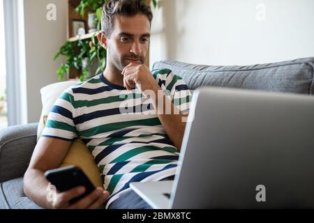 Young man sitting at home using a laptop and cellphone Stock Photo