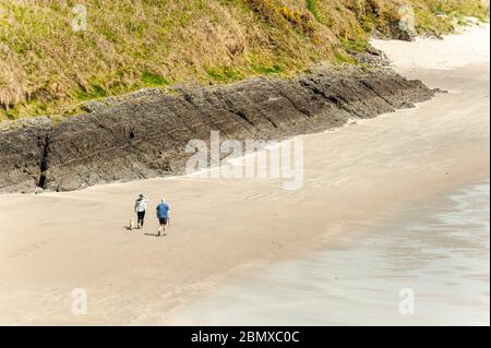 Inchydoney, West Cork, Ireland. 11th May, 2020. A couple walk their dog alone on the beach at Inchydoney in West Cork on a day of sunshine and high winds. Credit: AG News/Alamy Live News Stock Photo