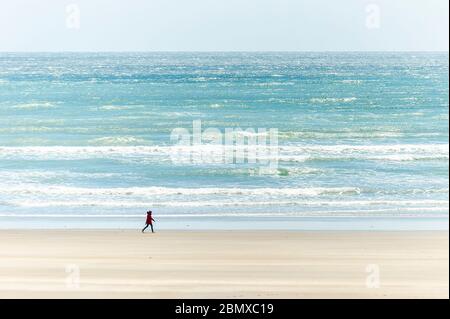 Inchydoney, West Cork, Ireland. 11th May, 2020. A woman walks alone on the beach at Inchydoney in West Cork on a day of sunshine and high winds. Credit: AG News/Alamy Live News Stock Photo