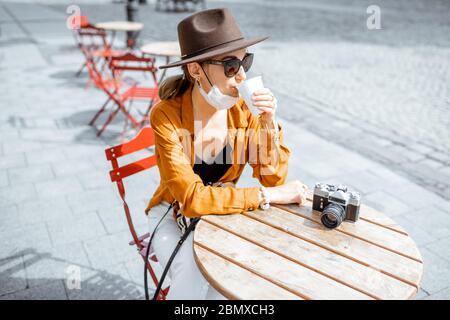 Young woman in facial mask sitting on the cafe terrace alone. Concept of social distancing and new social rules after coronavirus pandemic. Stock Photo