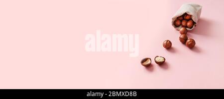 Top view of organic macadamia nuts dropped from burlap sack and place for text on pink background. Food concept Stock Photo