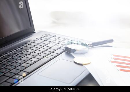 Laptop, bitcoin, magnifier and charts on the table. Business still life. Stock Photo