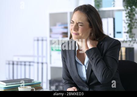 Executive woman with neckache complaining sitting on a desk at office Stock Photo