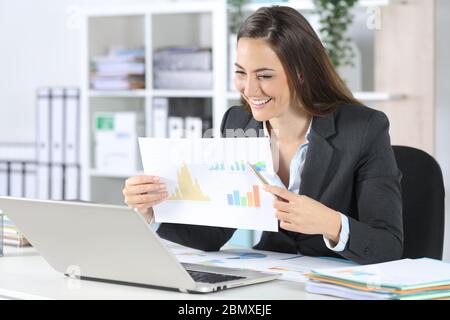Happy executive woman shows good results in graph report on videocall on laptop sitting on her desk at office Stock Photo