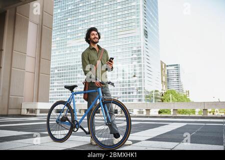 young man with blue cycle standing using smartphone while looking away Stock Photo