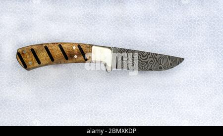 A beautiful fixed blade damascus knife featuring a zebra pattern is displayed over grey and white fabric. The unique handle is made of Myrtle Wood. Bo Stock Photo