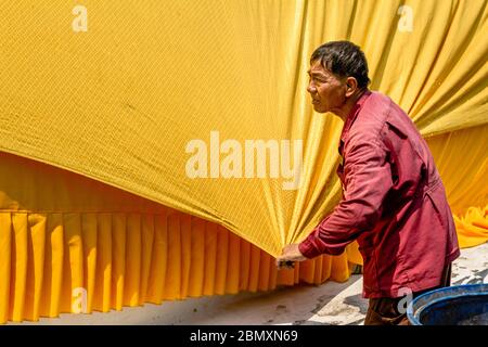 Old thai man stretches a yellow gaudy robe of a giant laying Buddha statue in Ayutthaya, Thailand, Asia Stock Photo