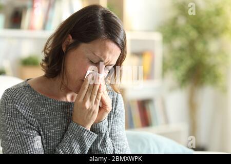 Sick adult woman blowing nose with tissue sitting on the couch at home Stock Photo