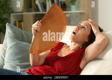 Adult woman fanning suffering heat stroke sitting in the livingroom at home Stock Photo