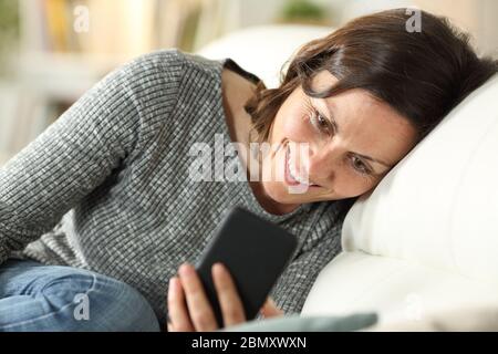 Happy adult woman checking smart phone relaxing sitting on a couch at home Stock Photo