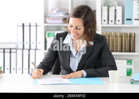Happy executive lady signing contract sitting on a desk at the office Stock Photo