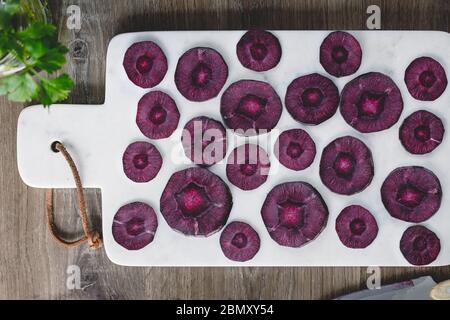 Overhead view on slices of raw purple carrot on a white marble board over kitchen table. Stock Photo