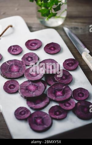 Slices of purple carrot on a white marble board over kitchen table. Stock Photo