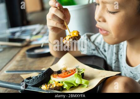 The boy eating hamburger black pork on the plate on a wooden table. Stock Photo