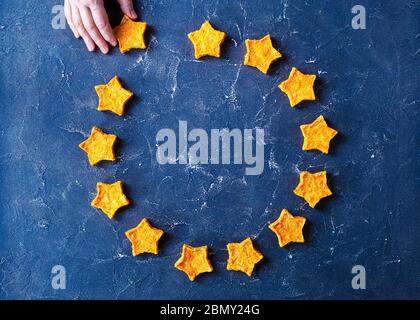 logo of the European Union of sweet Carrot Stars cookies on a blue concrete table, woman hand takes away one cookie, Brexit symbol, horizontal view fr Stock Photo