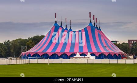 Circus tent with pink and blue striped on green lawn under summer sky. Venue accomodation used on summer festival. Stock Photo