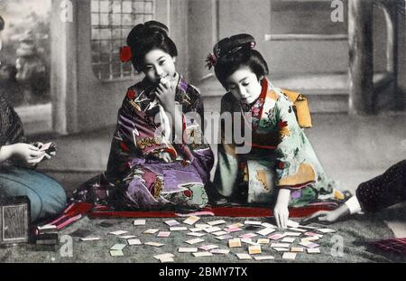 [ 1910s Japan - Japanese Women Playing Karuta ] —   Young Japanese women in kimono and traditional hairdo playing Karuta.  One person reads part of a poem on a yomifuda (reading) card, while others try to be the first to get the corresponding torifuda (grabbing) cards with the rest of the poem.  This postcard was published sometime between March 1907 (Meiji 40) and March 1918 (Taisho 7).  20th century vintage postcard. Stock Photo