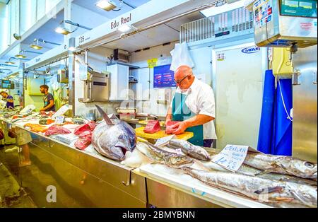 CADIZ, SPAIN - SEPTEMBER 24, 2019: The old fishmonger cuts tuna filet on his market table in Mercado Central de Abastos, on September 24 in Cadiz Stock Photo