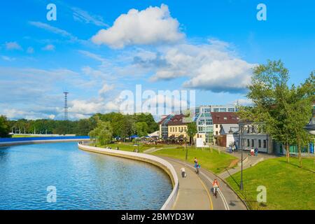 MINSK, BELARUS - JULY 17, 2019: People walking and cycling by Svisloch river embankment in bright sunny daytime, green park and city architecture in b Stock Photo