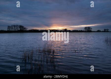A flash of sunset through the thick evening clouds over a calm lake with reeds Stock Photo
